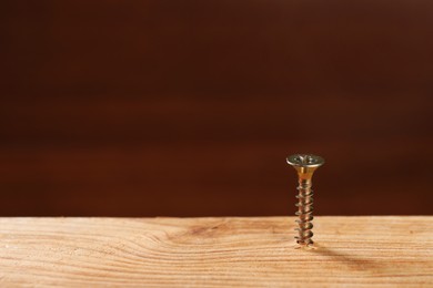 Photo of Screw in wooden plank against brown background, space for text