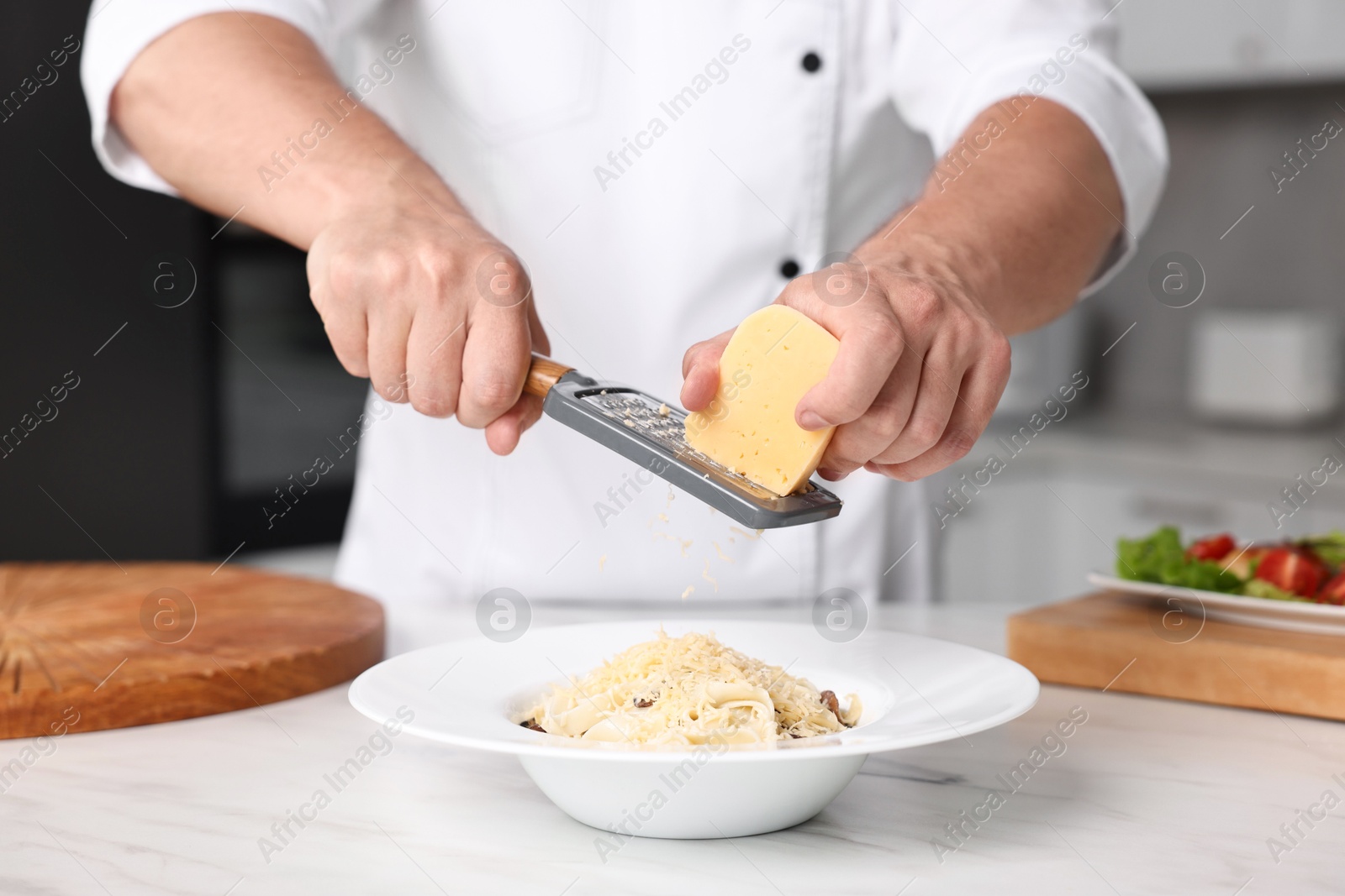 Photo of Professional chef grating cheese into delicious dish at white marble table in kitchen, closeup