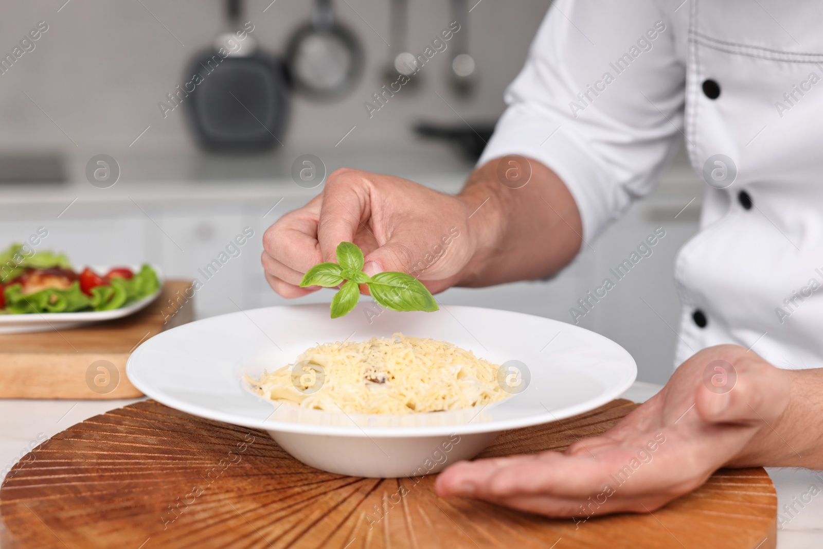 Photo of Professional chef decorating delicious pasta with basil at table in kitchen, closeup