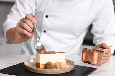 Professional chef smearing delicious cake with chocolate cream at white marble table in kitchen, closeup