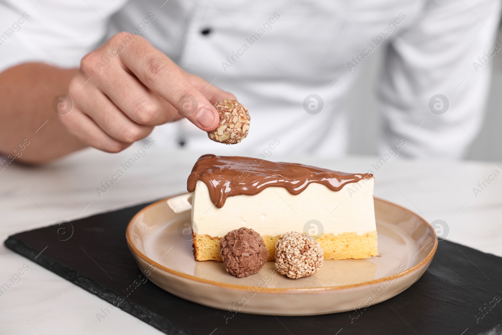 Photo of Professional chef decorating delicious cake with candy at table in kitchen, closeup