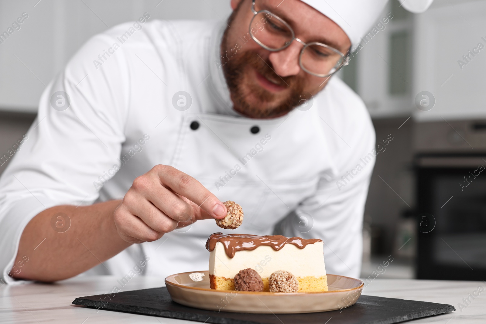 Photo of Professional chef decorating delicious cake with candy at table in kitchen