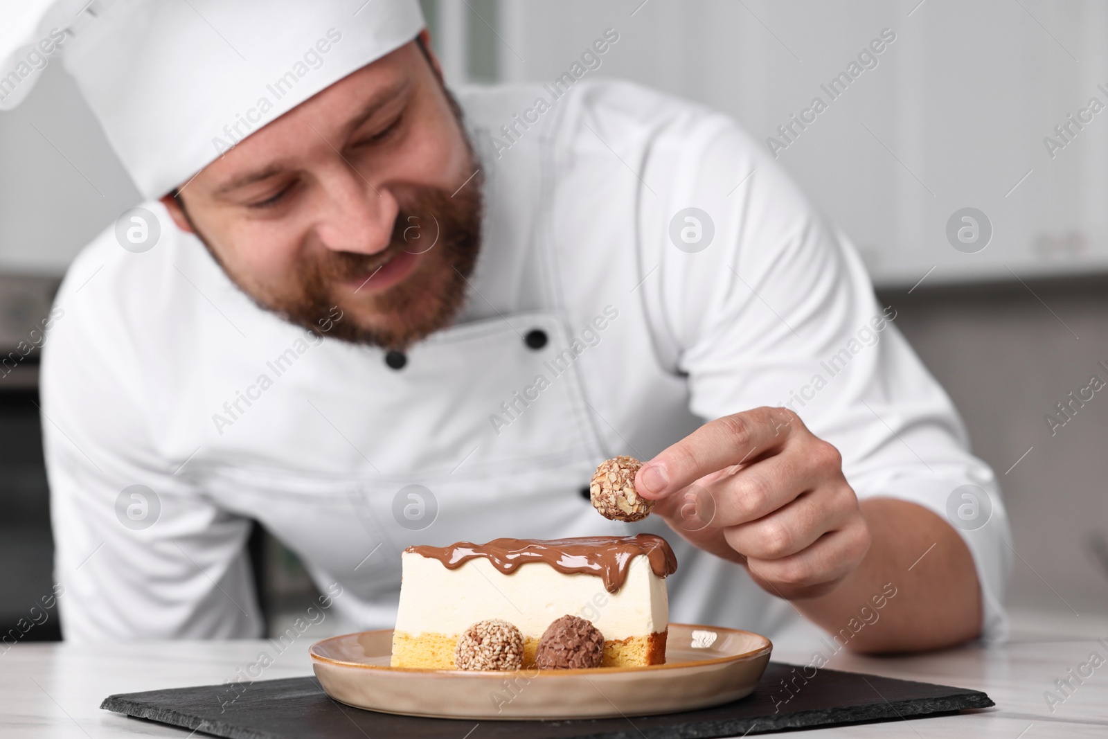 Photo of Professional chef decorating delicious cake with candy at table in kitchen