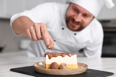 Photo of Professional chef decorating delicious cake with candy at table in kitchen, selective focus