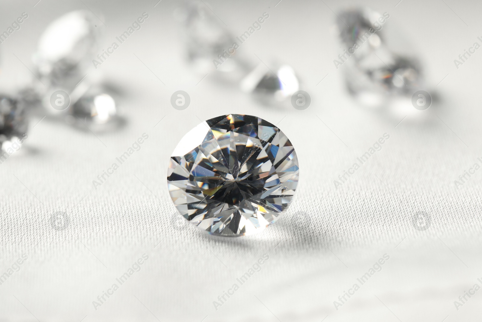 Photo of One beautiful shiny diamond on white fabric, closeup