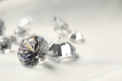 Photo of Many beautiful shiny diamonds on white fabric, closeup. Space for text