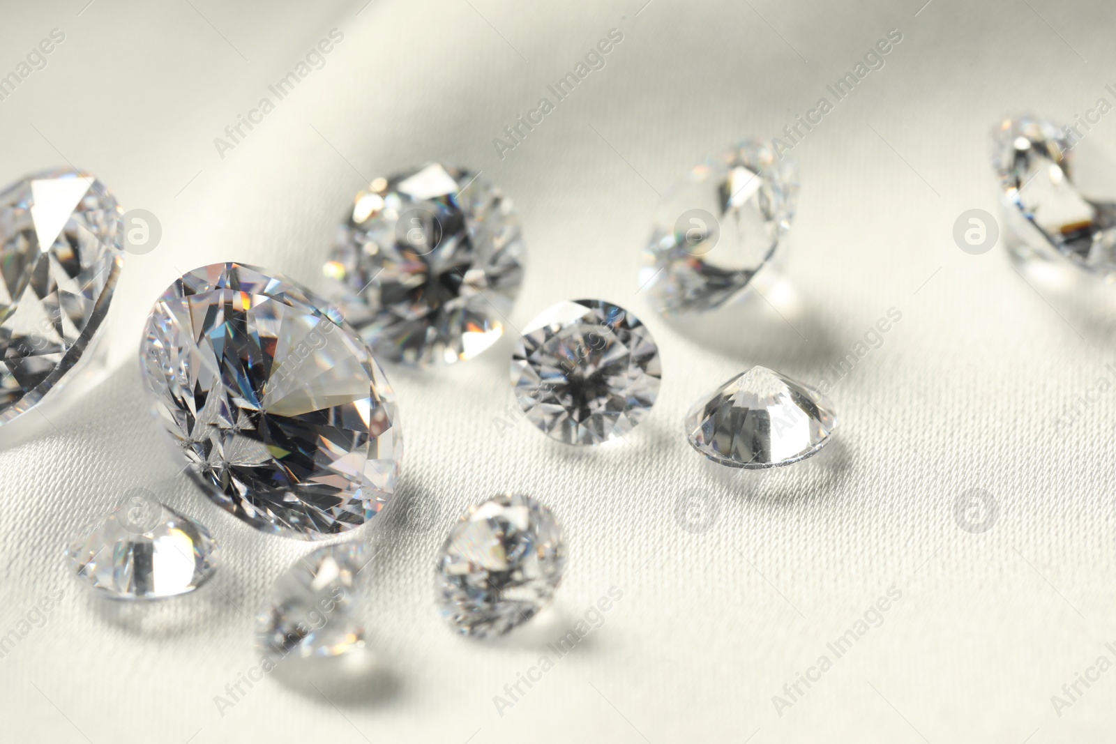 Photo of Many beautiful shiny diamonds on white fabric, closeup