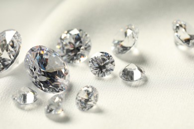 Photo of Many beautiful shiny diamonds on white fabric, closeup