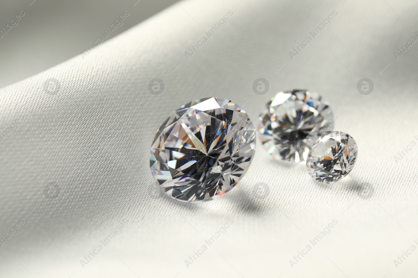 Photo of Three beautiful shiny diamonds on white fabric, closeup