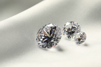 Three beautiful shiny diamonds on white fabric, closeup