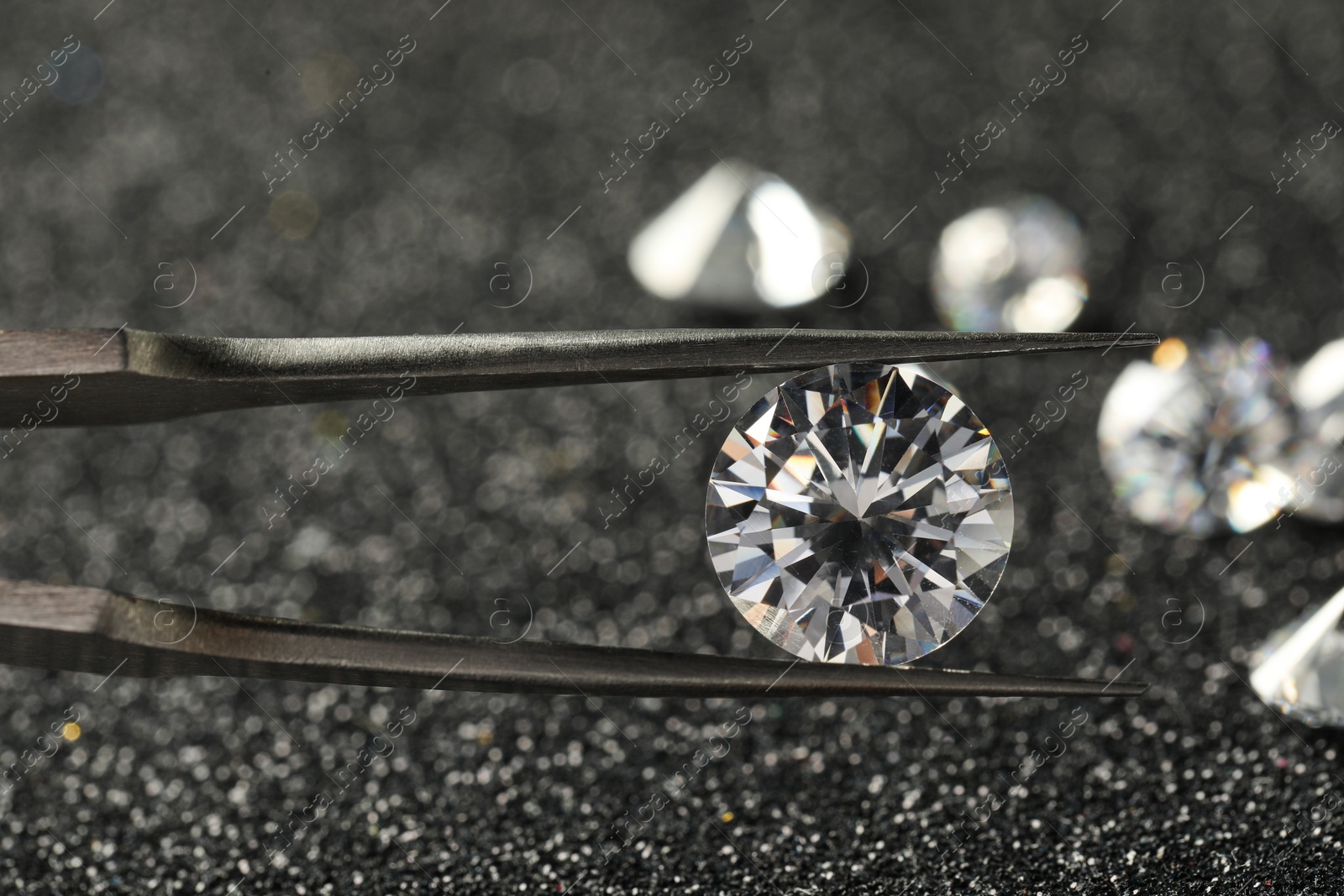 Photo of Tweezers with beautiful diamond on dark shiny background, closeup