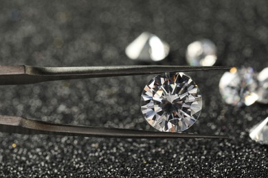 Photo of Tweezers with beautiful diamond on dark shiny background, closeup