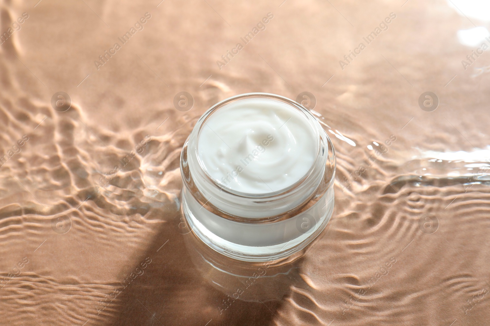 Photo of Jar with face cream in water on beige background