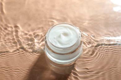 Jar with face cream in water on beige background