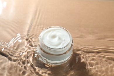 Jar with face cream in water on beige background