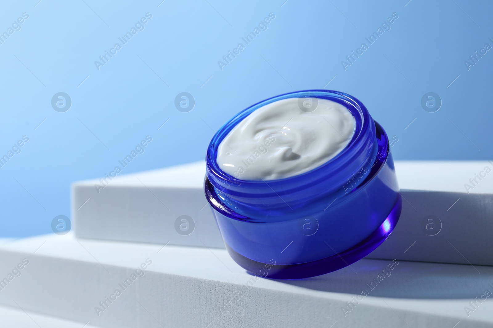 Photo of Stylish presentation of face cream in jar against light blue background, closeup