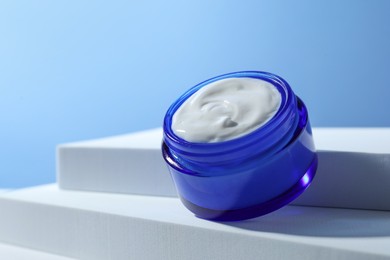 Stylish presentation of face cream in jar against light blue background, closeup