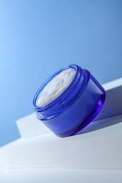 Photo of Stylish presentation of face cream in jar against light blue background