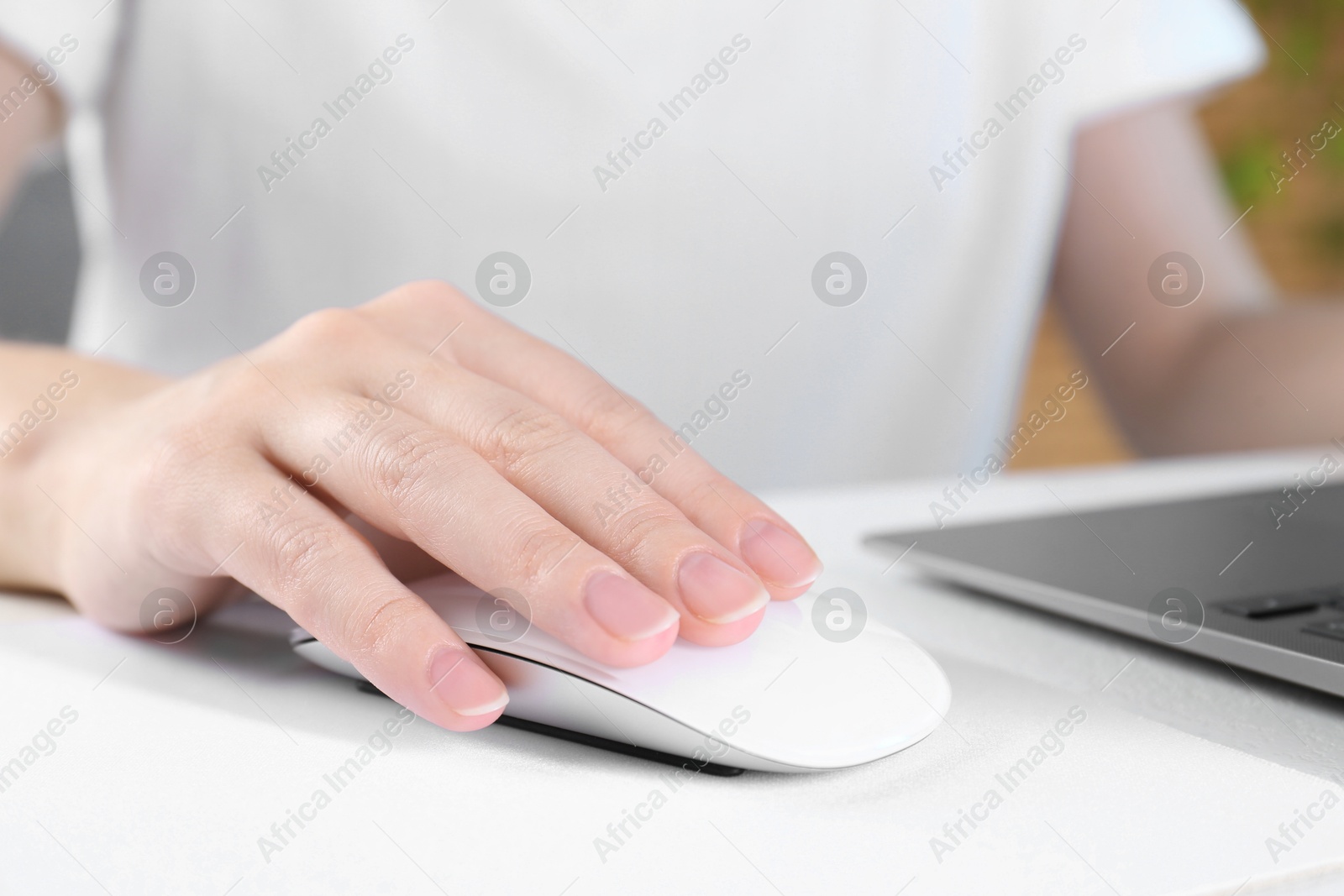 Photo of Woman using computer mouse while working with laptop at white table, closeup