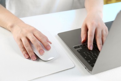 Photo of Woman using computer mouse while working with laptop at white table, closeup