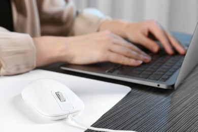 Photo of Woman working with laptop at black wooden table, focus on computer mouse