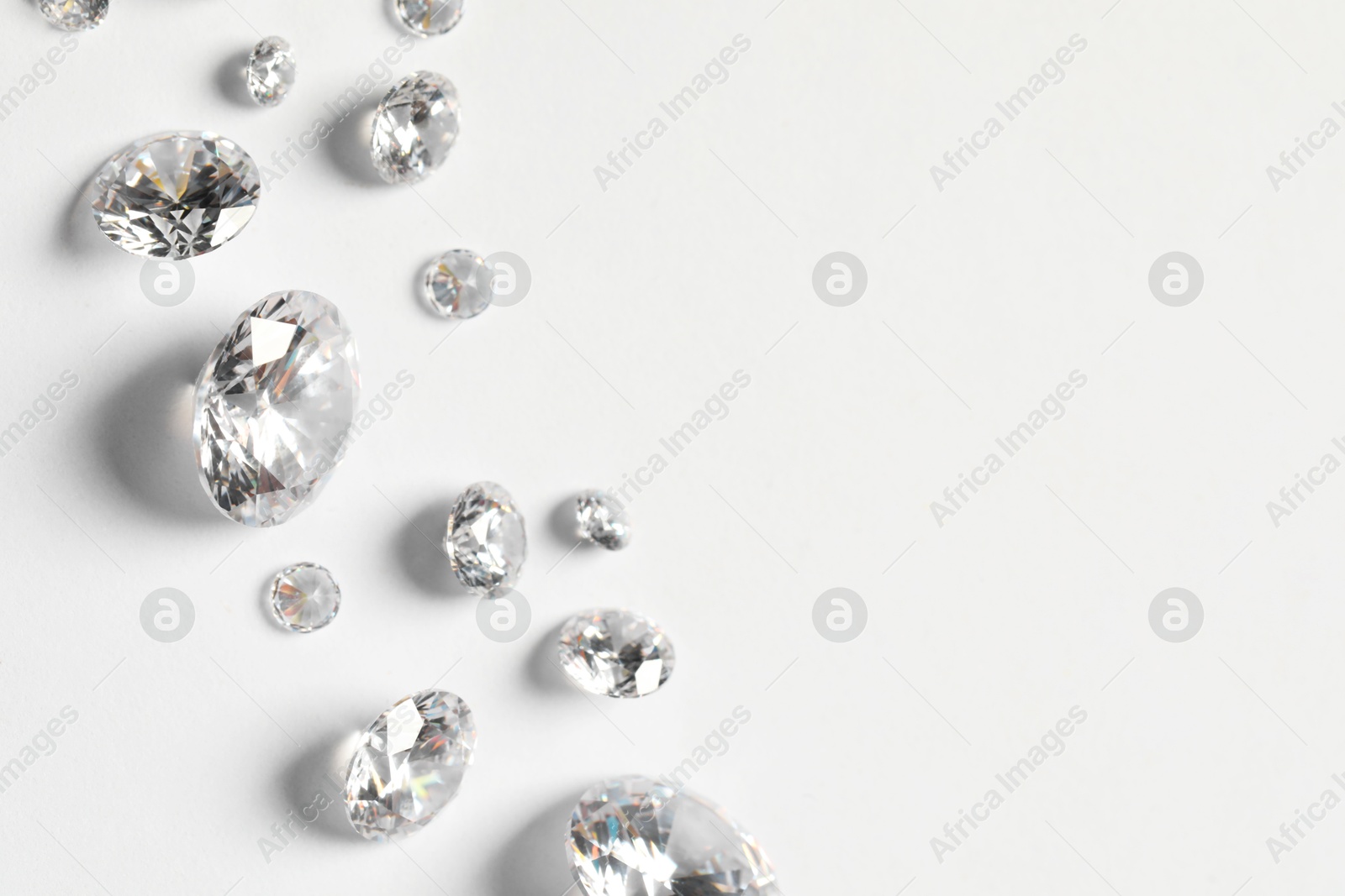 Photo of Many beautiful shiny diamonds on white background, flat lay. Space for text