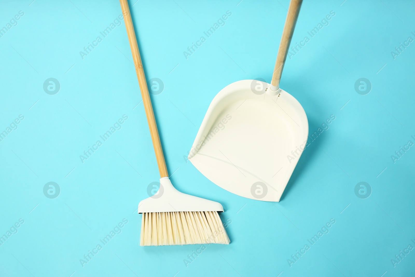 Photo of Cleaning broom and dustpan on light blue background, flat lay