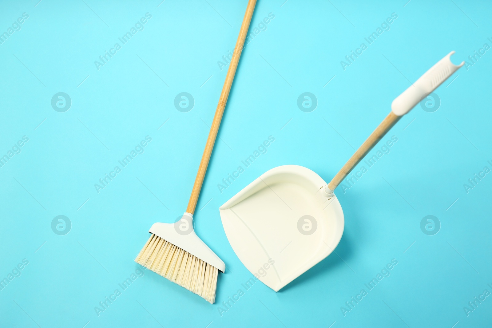 Photo of Cleaning broom and dustpan on light blue background, flat lay