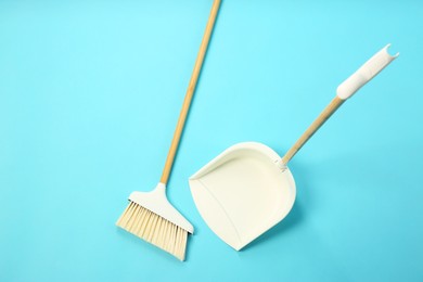 Photo of Cleaning broom and dustpan on light blue background, flat lay