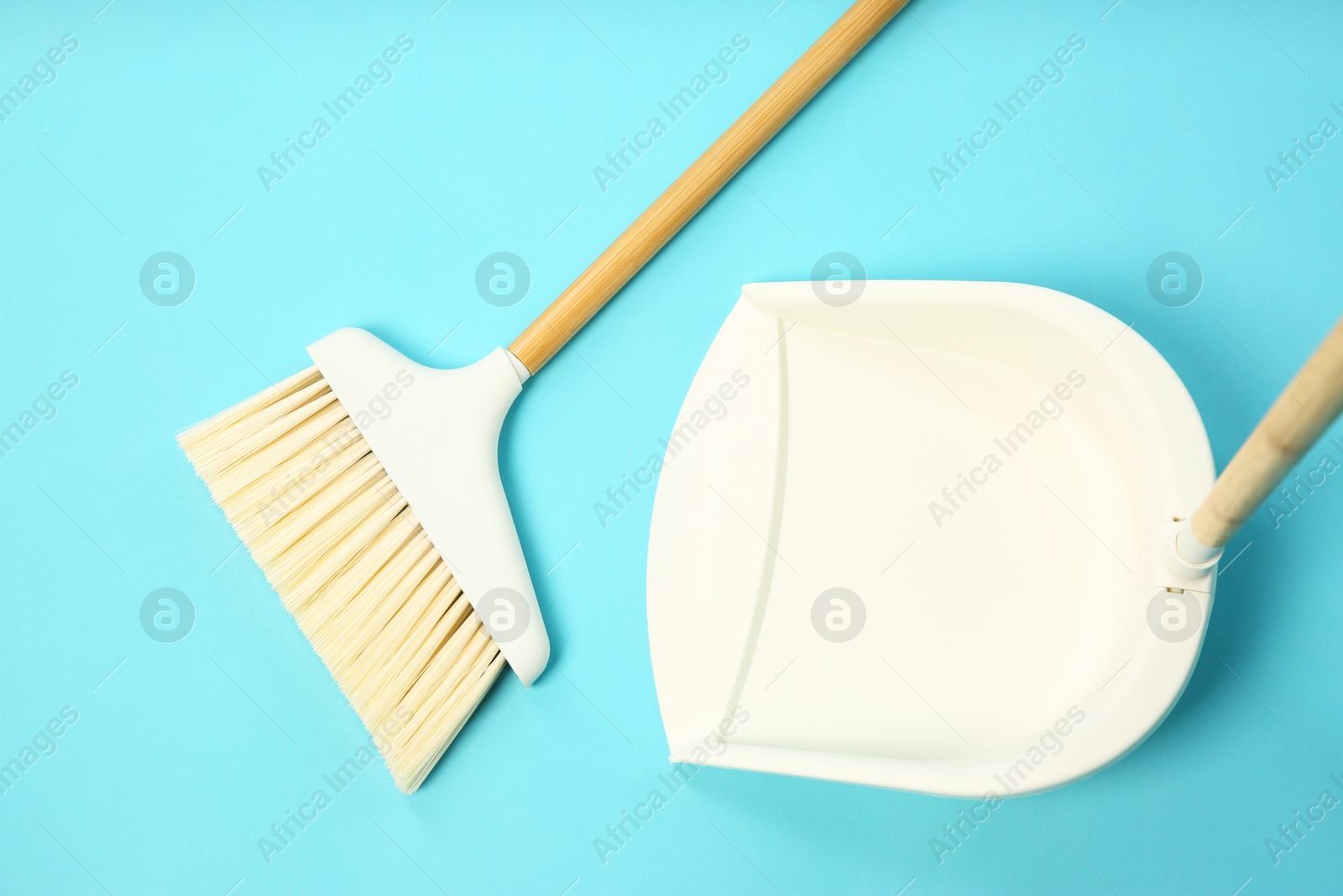 Photo of Cleaning broom and dustpan on light blue background, flat lay