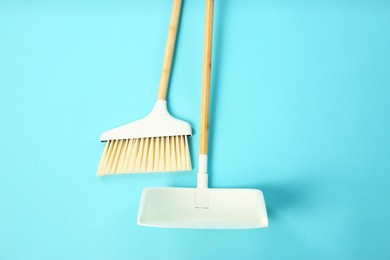 Photo of Cleaning broom and dustpan on light blue background, flat lay