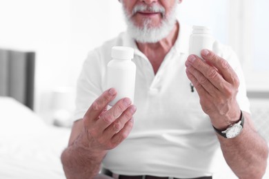 Senior man with bottles of pills indoors, closeup