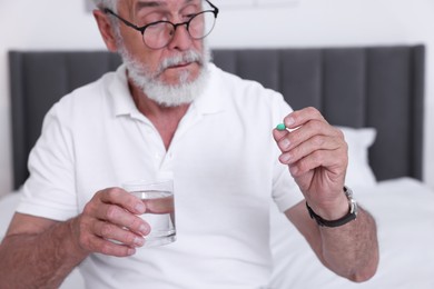 Senior man with glass of water and pill on bed at home, closeup