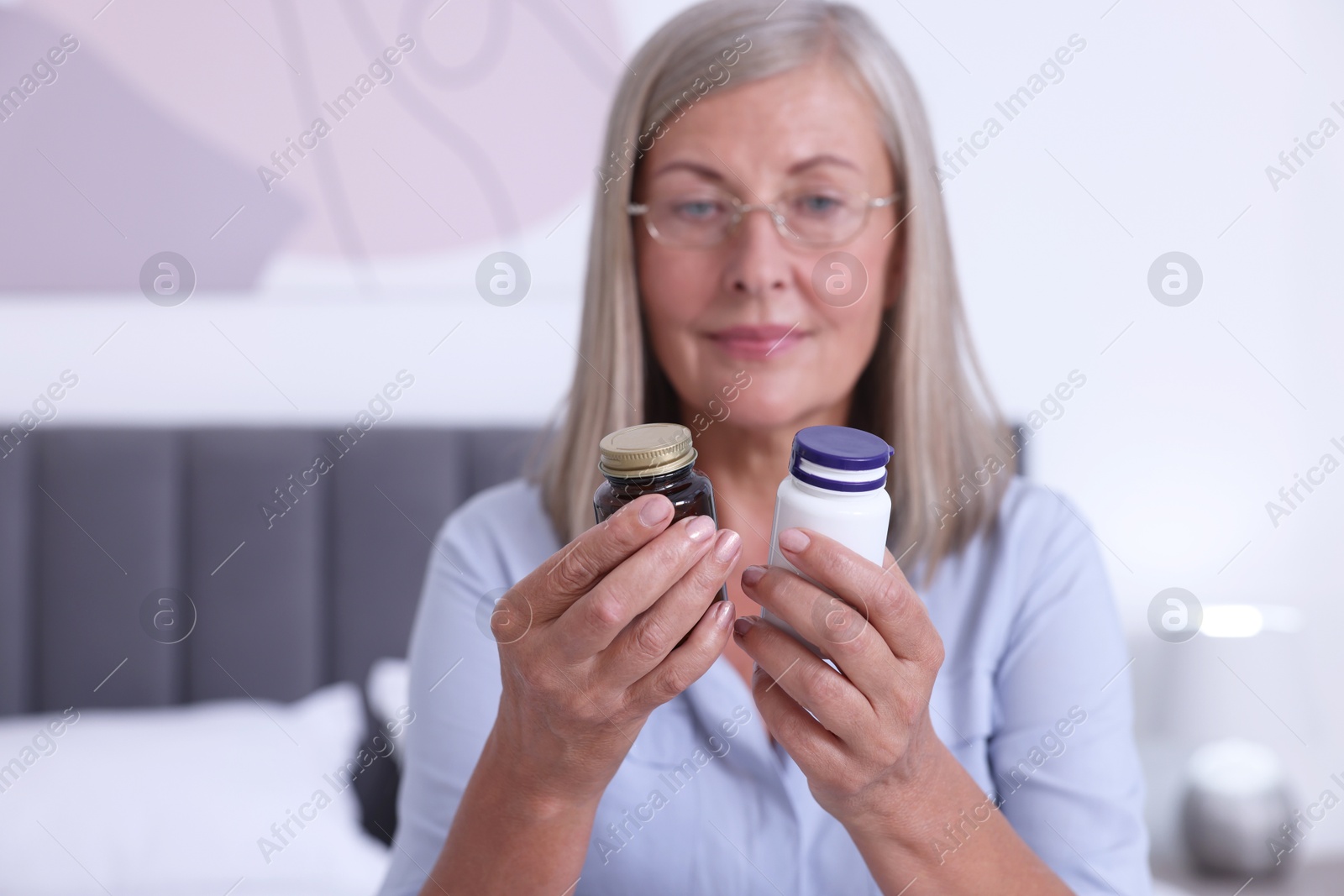 Photo of Senior woman with bottles of pills indoors, selective focus