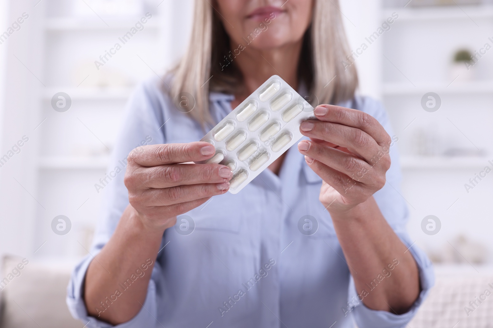 Photo of Senior woman holding blister with pills at home, closeup