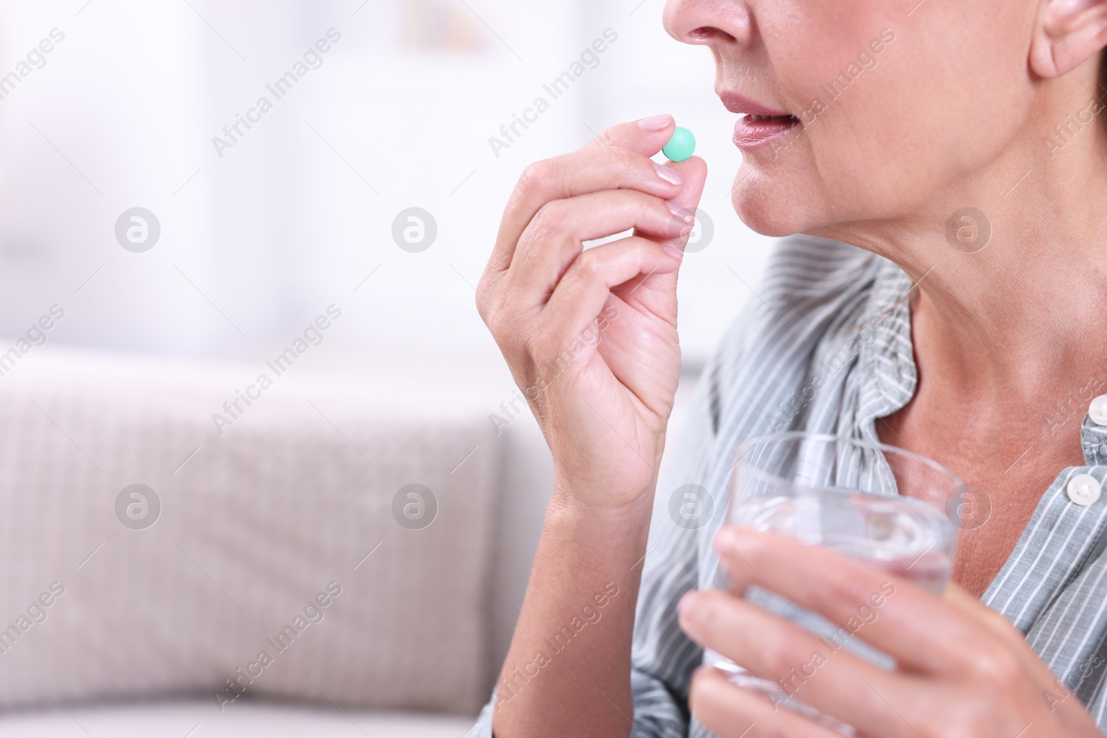 Photo of Senior woman with glass of water taking pill at home, closeup. Space for text