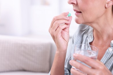 Photo of Senior woman with glass of water taking pill at home, closeup. Space for text