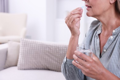 Photo of Senior woman with glass of water taking pill at home, closeup. Space for text