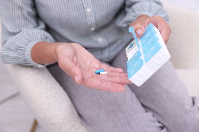 Photo of Senior woman with pills and organizer in armchair at home, closeup