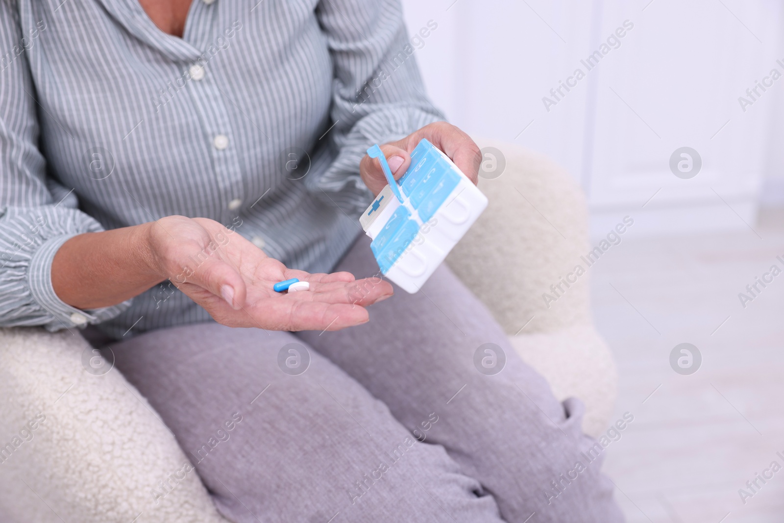 Photo of Senior woman with pills and organizer in armchair at home, closeup. Space for text