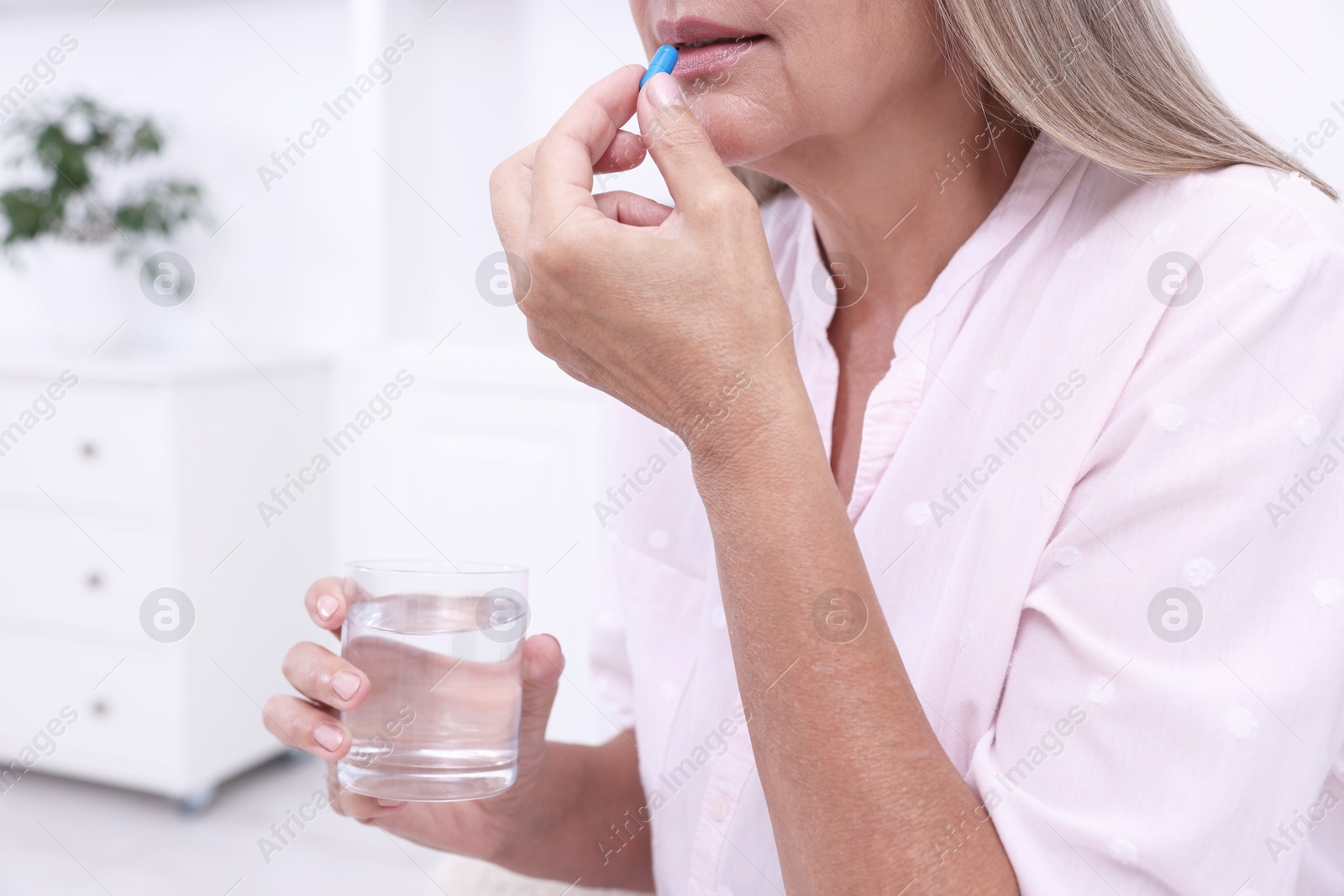 Photo of Senior woman with glass of water taking pill at home, closeup