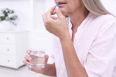 Senior woman with glass of water taking pill at home, closeup