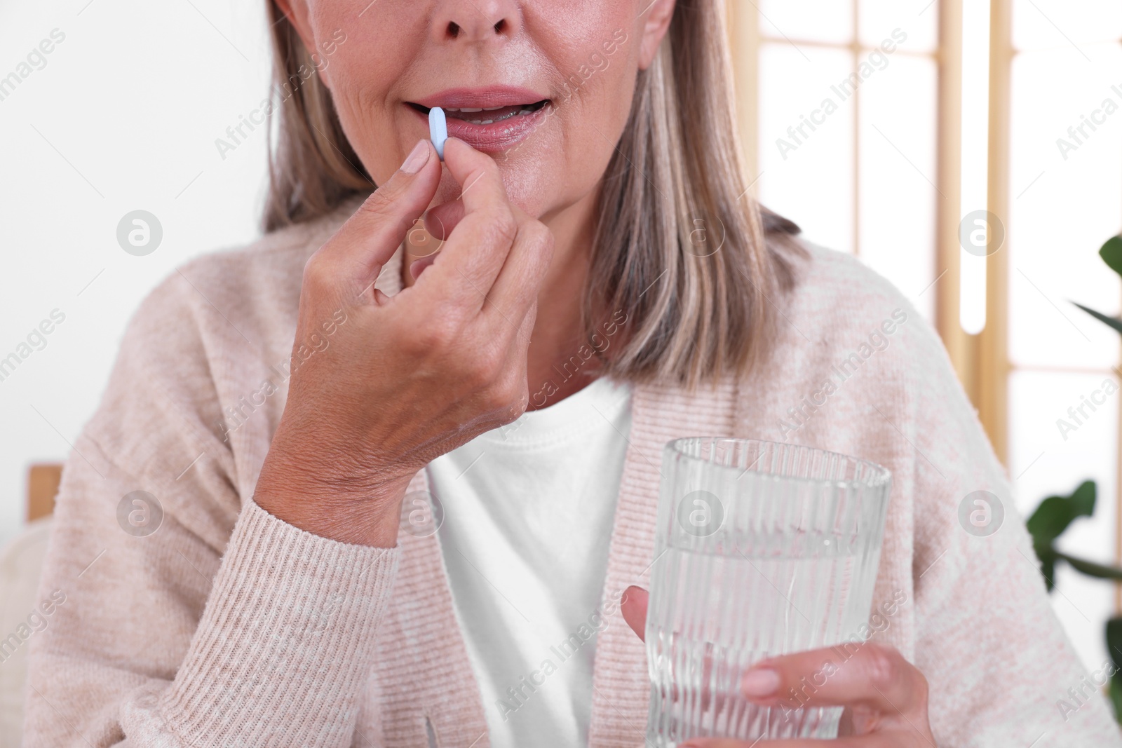 Photo of Senior woman with glass of water taking pill at home, closeup