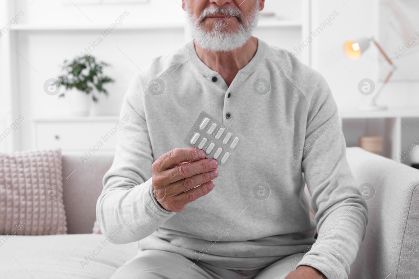 Photo of Senior man holding blister with pills at home, closeup