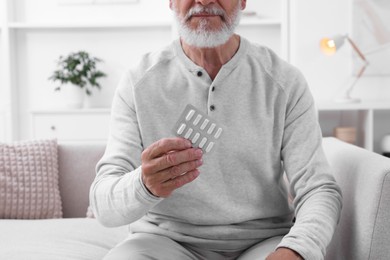 Senior man holding blister with pills at home, closeup