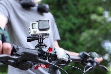 Photo of Man riding bicycle with modern action camera outdoors, closeup