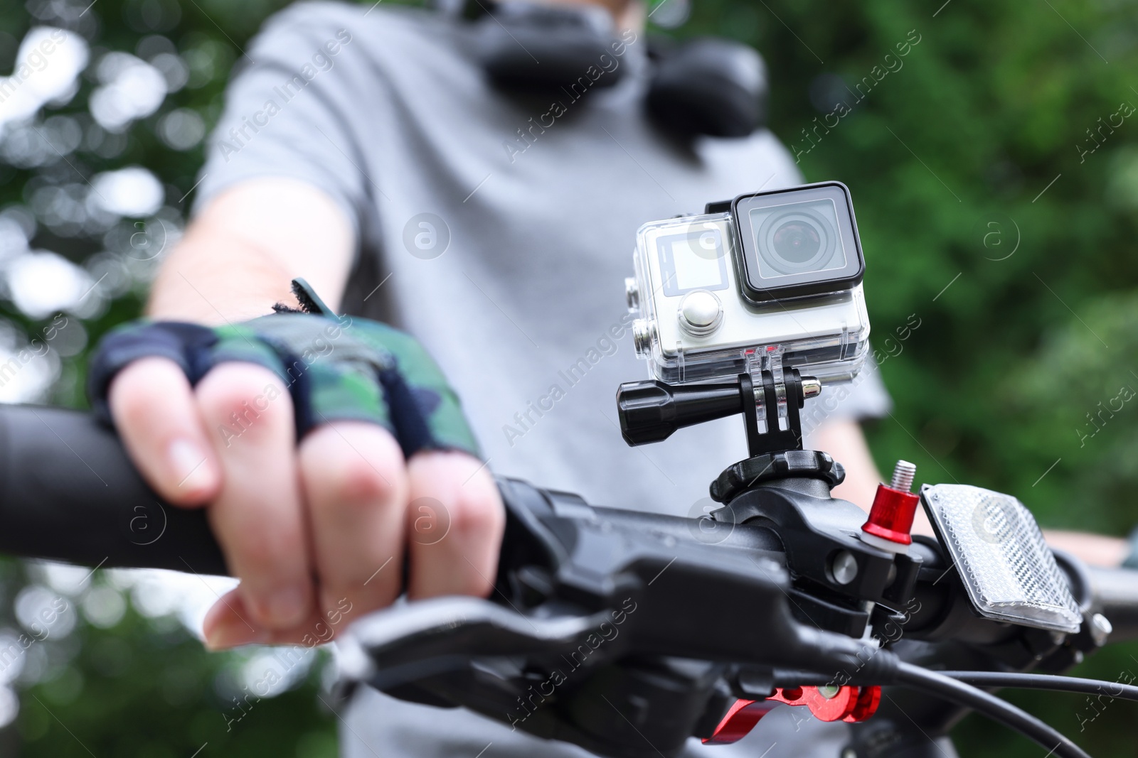 Photo of Man riding bicycle with modern action camera outdoors, closeup