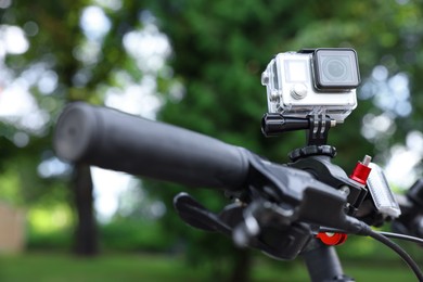 Photo of Modern action camera with mount on bicycle outdoors, closeup