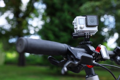 Photo of Modern action camera with mount on bicycle outdoors, closeup