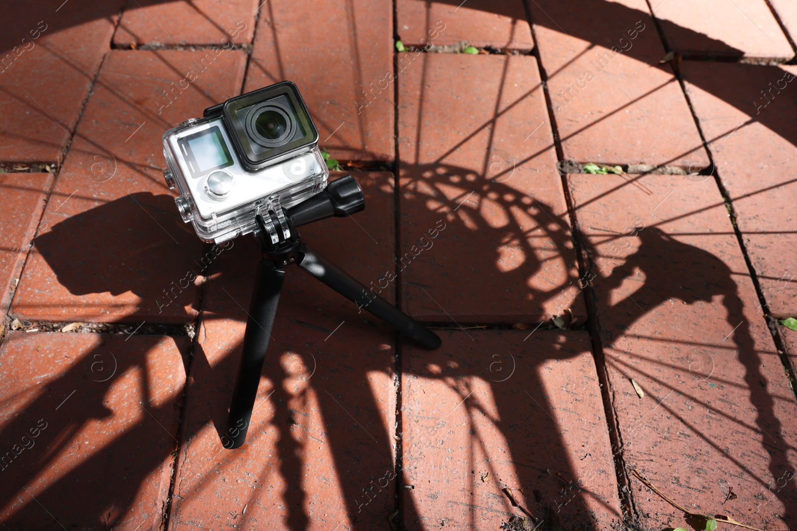 Photo of Modern action camera with tripod on pavement outdoors, above view. Space for text